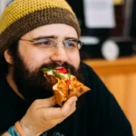 A man wearing cap and eating pizza slice