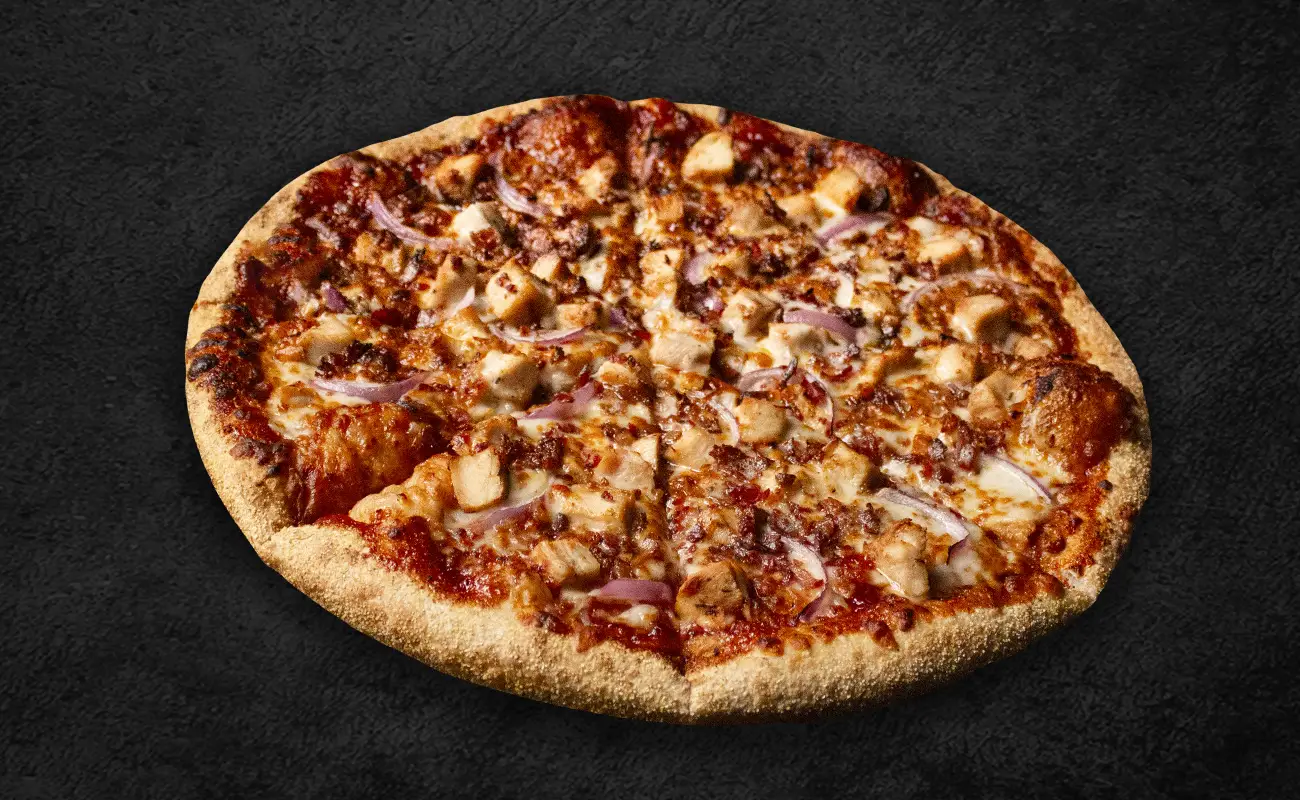 A baked pizza topped with chunks of grilled chicken, sliced red onions, melted cheese, and a tangy tomato-based sauce on a golden, crispy crust.