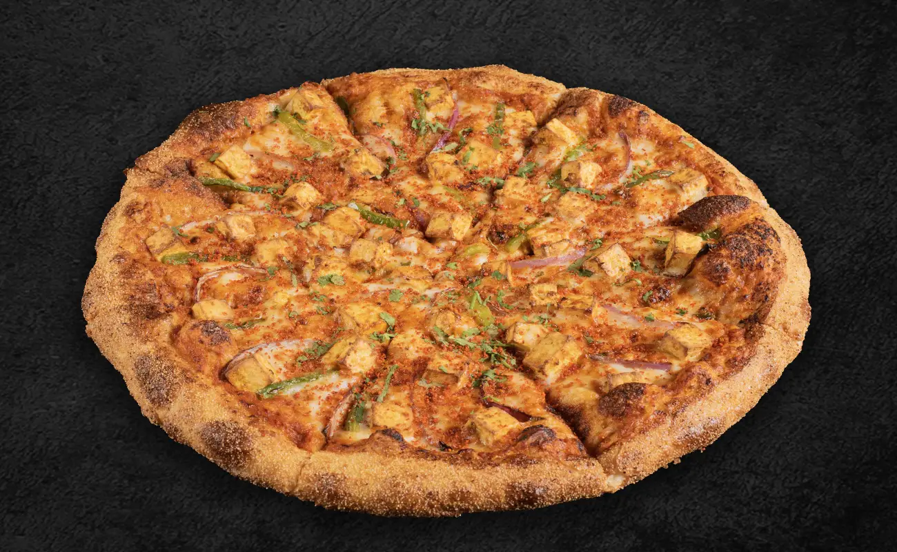 A freshly baked Indian-style pizza topped with marinated paneer cubes, sliced red onions, green bell peppers, and a blend of Indian spices on a golden-brown crust.