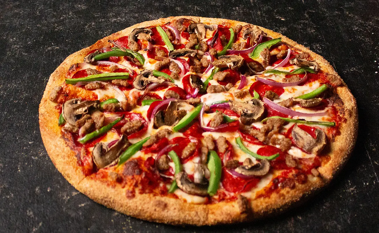 Pizzawala's deluxe work pizza. A freshly baked pizza topped with green bell peppers, red onions, mushrooms, sausage, and pepperoni, placed on a dark textured surface.