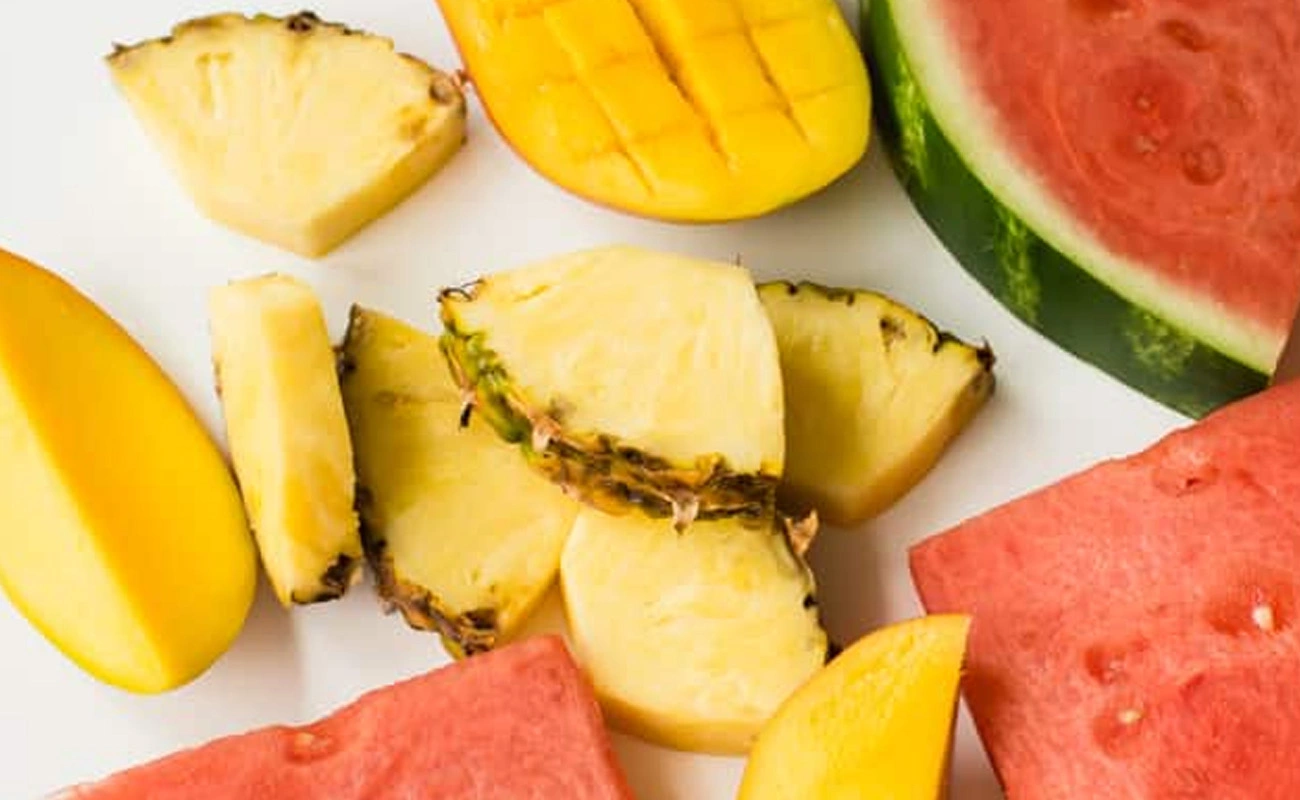 Freshly cut tropical fruits including pineapple slices, ripe mango, and watermelon pieces on a white background.