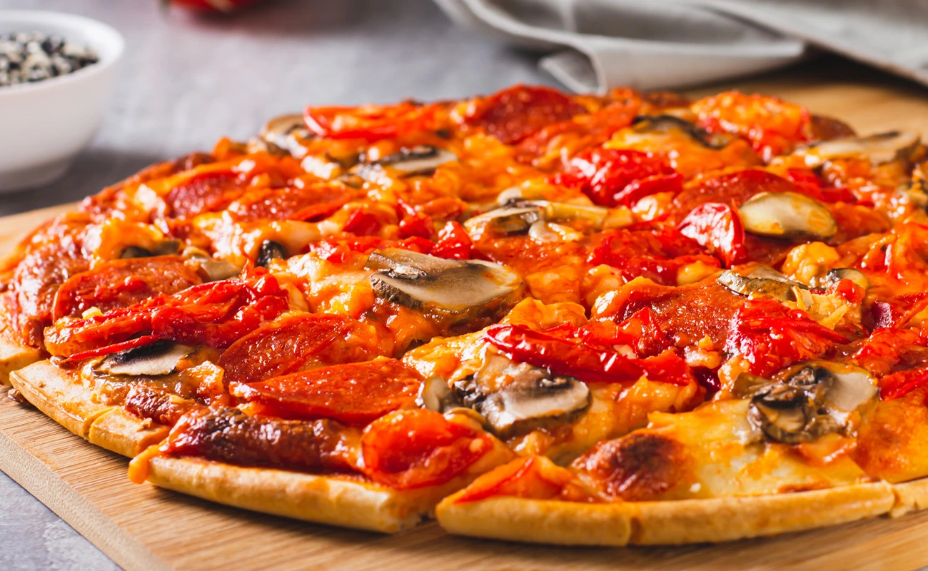St. Louis-style pizza with thin cracker-like crust, Provel cheese, pepperoni, mushrooms, and tomatoes cut into square slices.