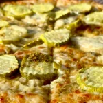 A close-up of a pizza featuring green pickle slices as a distinctive topping, adding a tangy twist.