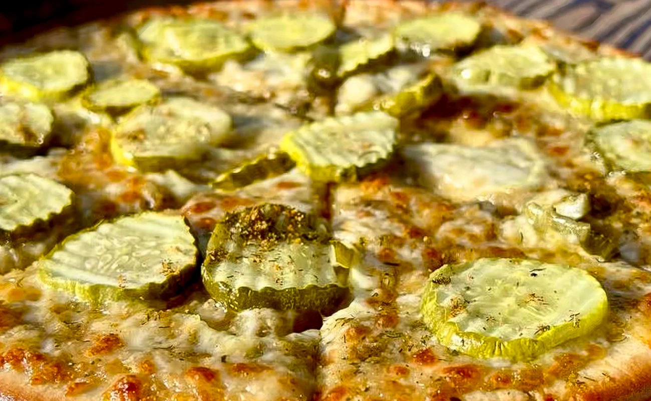 A close-up of a pizza featuring green pickle slices as a distinctive topping, adding a tangy twist.
