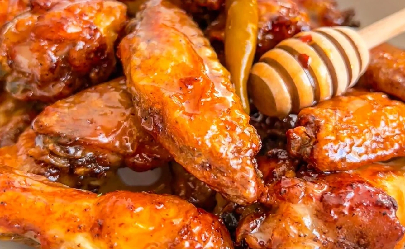 Hot honey chicken wings glazed with a sweet-heat sauce and a wooden dipper.