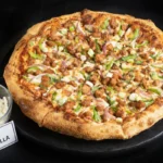 A black plate holds a pizza garnished with cheese and green onions.