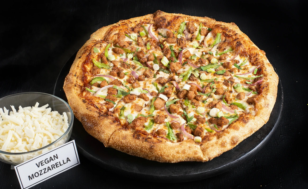 A black plate holds a pizza garnished with cheese and green onions.