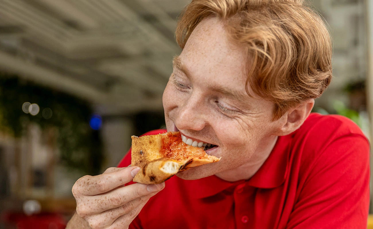 Smiling man enjoying a slice of cheesy pizza at a restaurant
