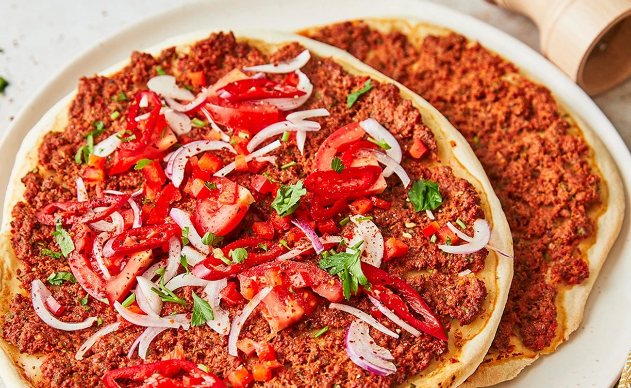Traditional Turkish lahmacun with spiced minced meat, topped with fresh tomatoes, onions, and parsley, served on a thin flatbread for an authentic meal.