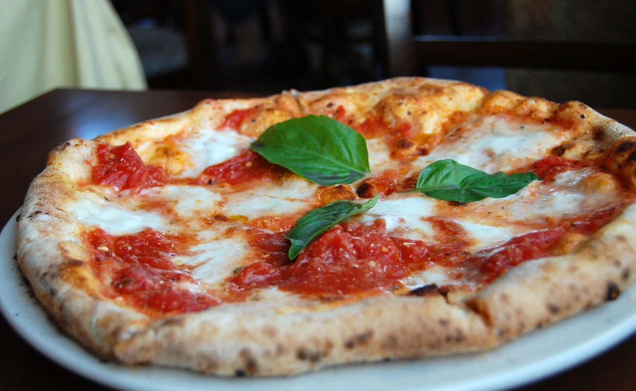 Classic Italian Margherita pizza with fresh tomato sauce, melted mozzarella, and basil leaves on a crispy crust, served on a white plate in a cozy restaurant setting.